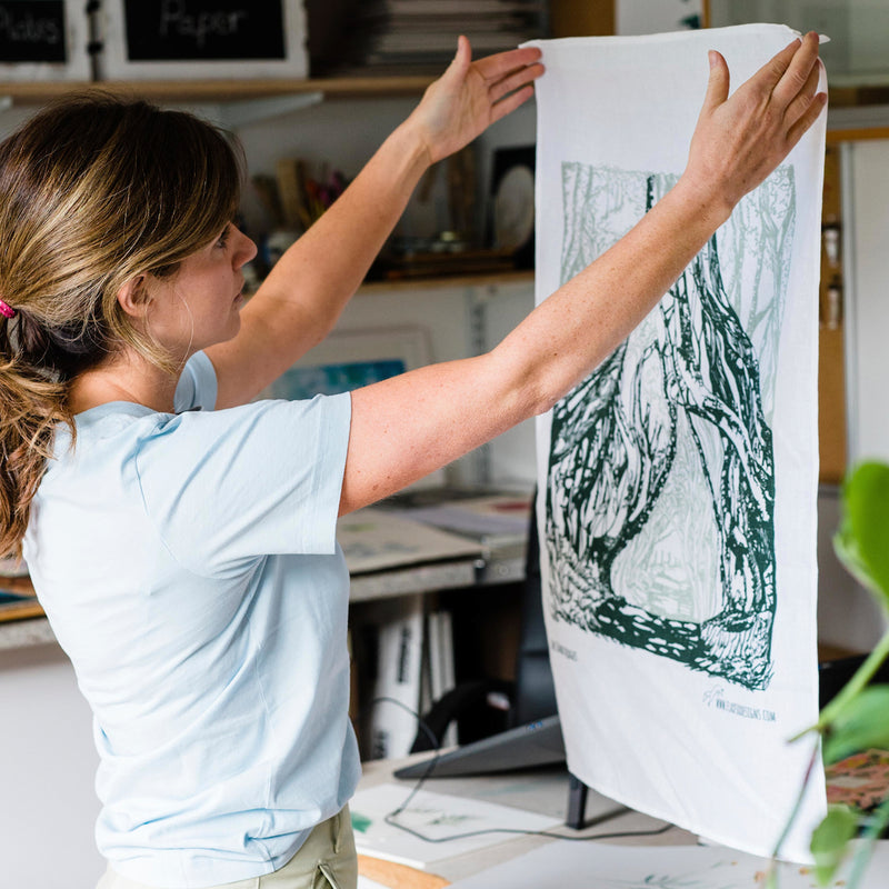 Danielle Morgan Belfast Artist holding up the Dark Hedges Linen Tea Towel